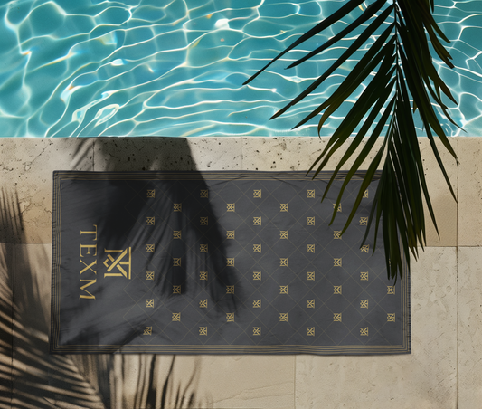 TEXM Heritage Charcoal & Gold beach towel laid on warm sand by the shore