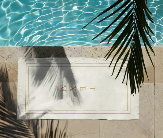 TEXM Ember Cream & Gold minimalist beach towel laid on warm sand by the shore