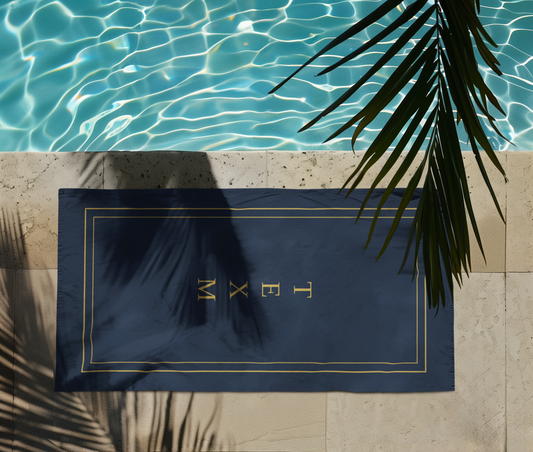 TEXM Ember Navy & Gold minimalist beach towel laid on warm sand by the shore